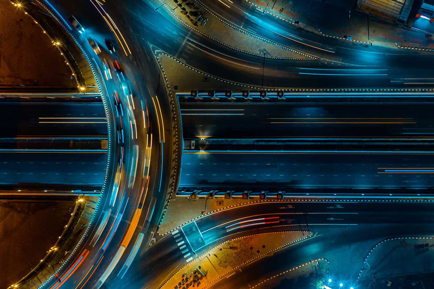 Overhead view of a multi-lane highway interchange at night with light trails of moving vehicles.