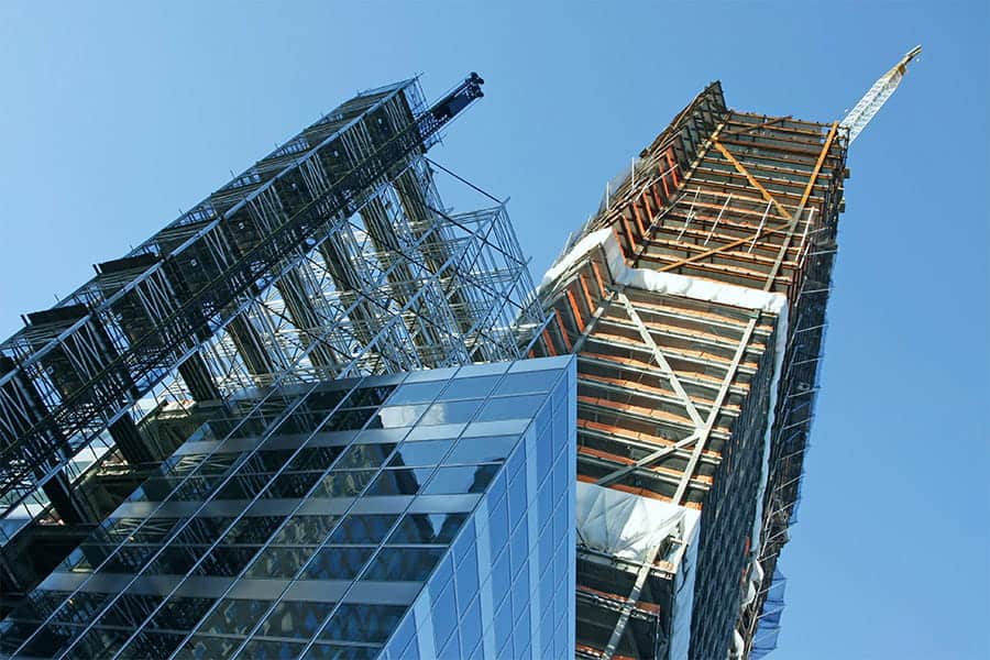 Skyscraper under construction with scaffolding and cranes against a clear blue sky.