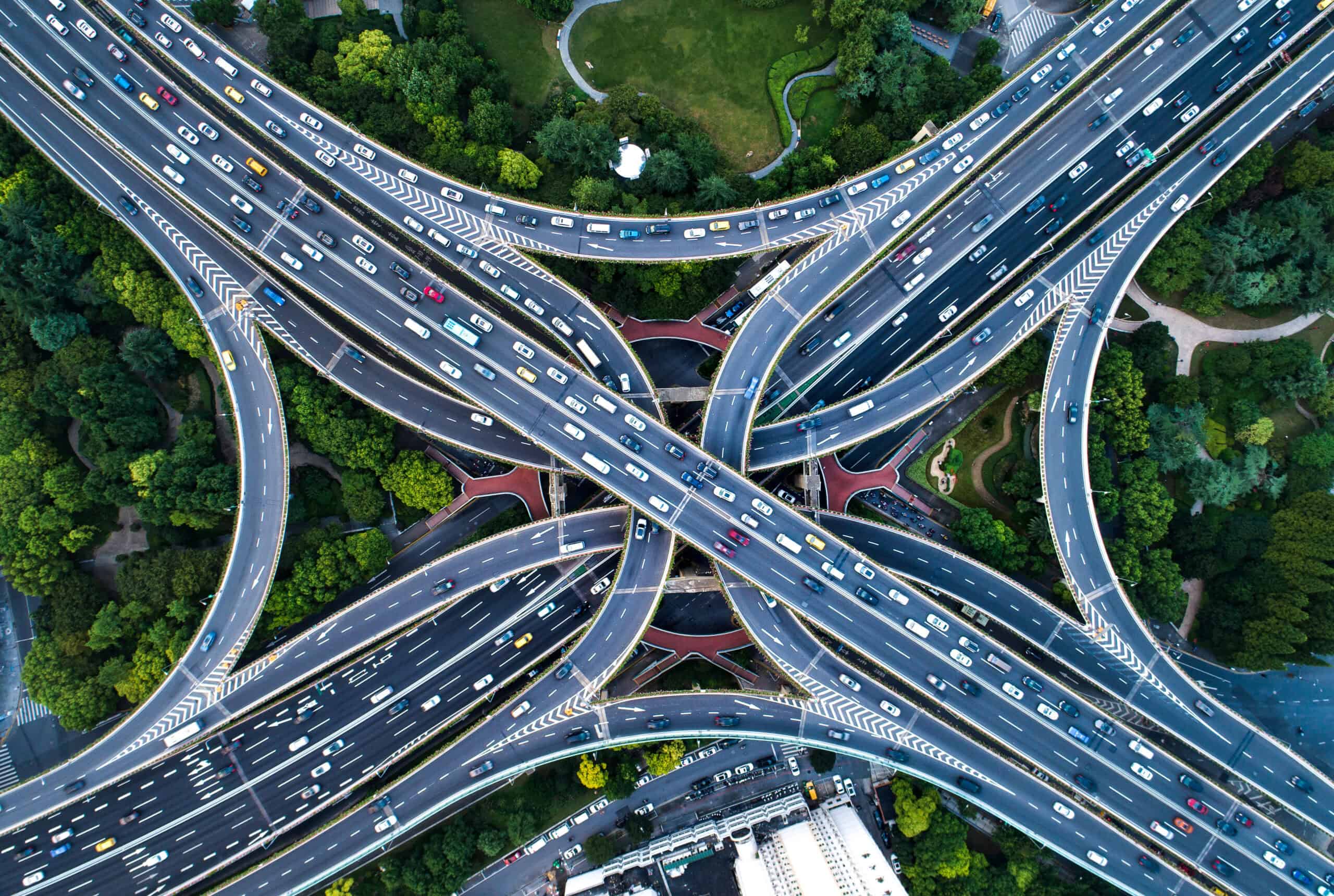 Aerial view of a complex multi-level highway interchange with numerous cars and surrounding green landscaping.