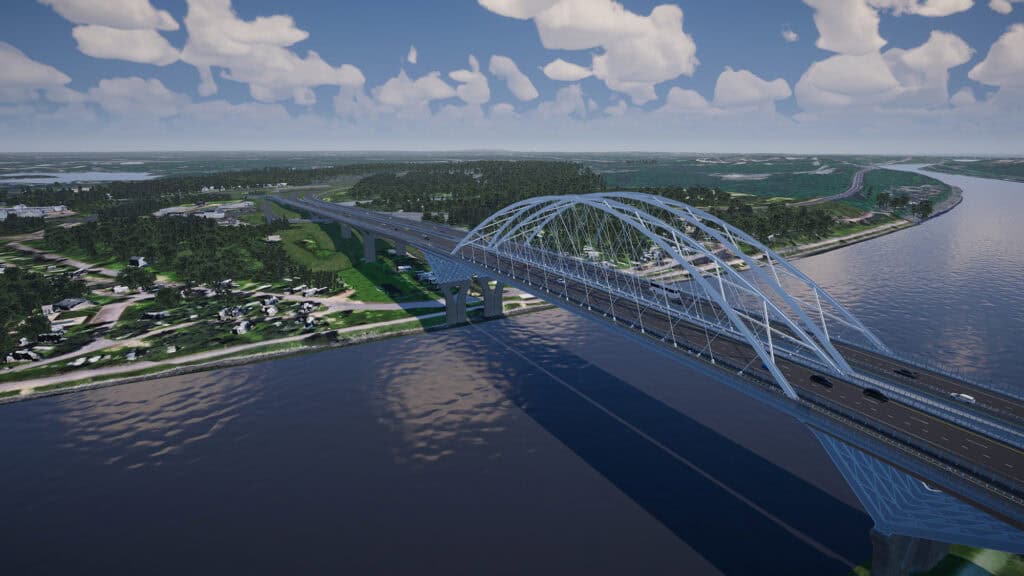 A large steel arch bridge spans a wide river, connecting two areas of green landscape under a partly cloudy sky. Vehicles are visible traveling across the bridge.
