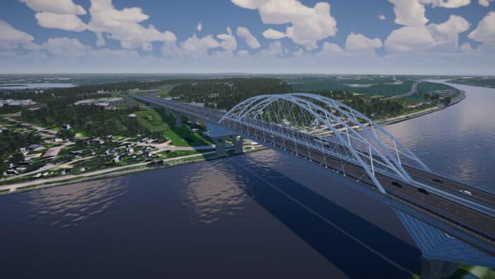 A large steel arch bridge spans a wide river, connecting two areas of green landscape under a partly cloudy sky. Vehicles are visible traveling across the bridge.