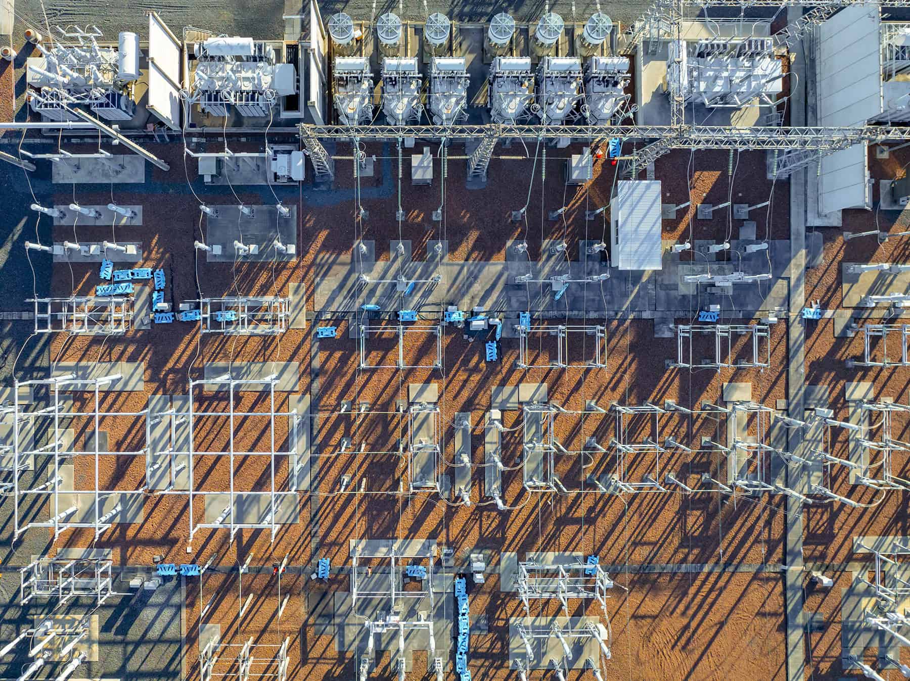 Aerial view of an electrical substation showing transformers, power lines, and metal frameworks casting long shadows—highlighting the vital role substations play in supporting the wind energy future from ambition to execution.