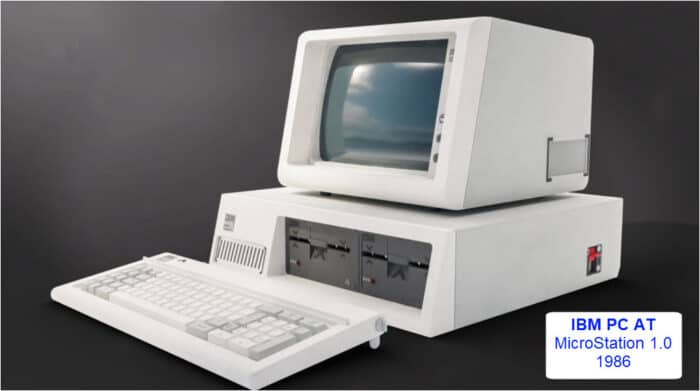 An IBM PC AT with an attached monitor, keyboard, and dual floppy disk drives. A label indicates it is running MicroStation 1.0 from 1986.