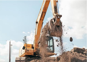 A yellow excavator, integral to land development, lifts a large scoop of dirt against a blue sky with scattered clouds.