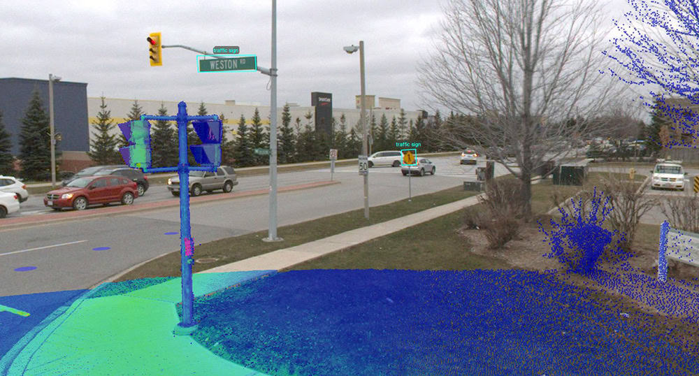 An intersection with traffic lights on a cloudy day. Cars are on the road, and various objects are annotated with colored points. Trees and buildings are in the background.