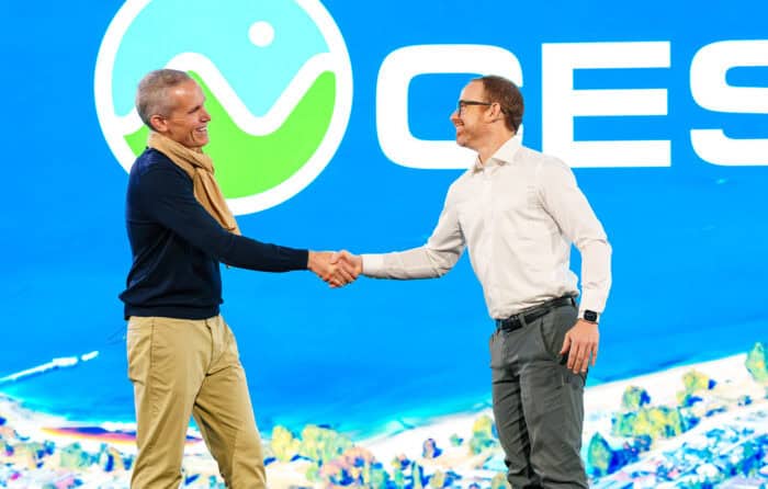 Julien Moutte, left, and Patrick Cozzi, right, shaking hands on a stage with a large Cesium logo in the background. One is wearing a navy sweater and beige scarf, the other a white shirt.