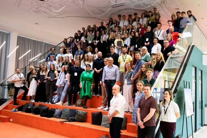 A large group of people stands on a staircase in an indoor setting, posing for a group photo.