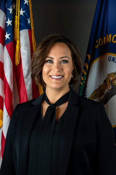 Kentucky Lt. Gov. Jacqueline Coleman stands in front of the U.S. and Kentucky state flags, smiling at the camera.