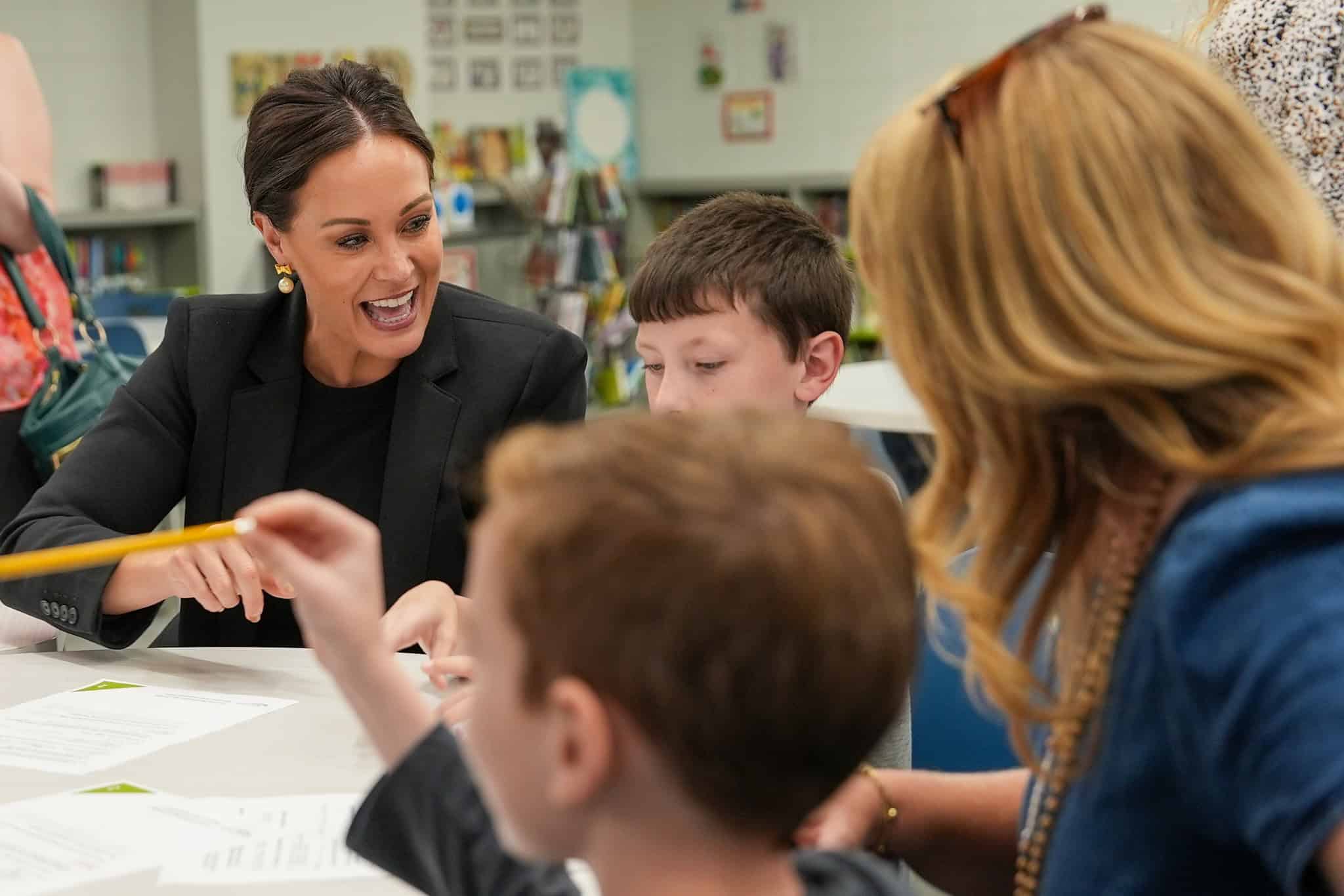 Kentucky Lt. Gov. Jacqueline Coleman talks with two children and another adult at a table covered with papers in a classroom or library setting.