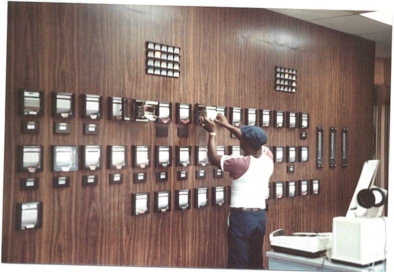 Person adjusting equipment on a wall full of electrical panels in a vintage setting.