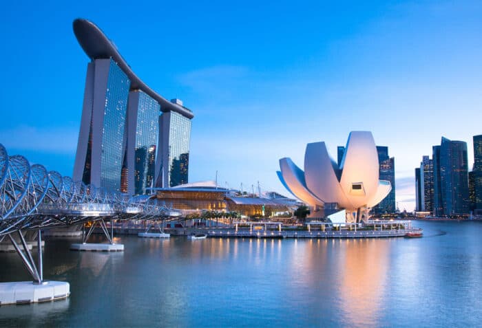 View of Marina Bay Sands, Helix Bridge, and the lotus-shaped ArtScience Museum in Singapore at dusk, with skyline buildings in the background and water in the foreground.