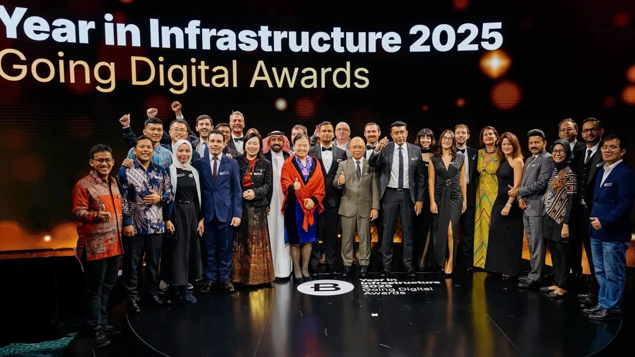 A large group of people pose on stage in formal attire in front of a screen displaying "Year in Infrastructure 2025 Going Digital Awards.
