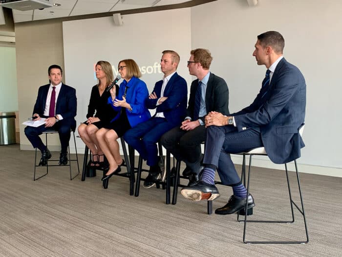 Seated are six people in business attire during a presentation.