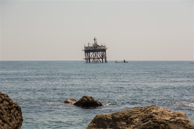 An offshore oil platform stands in the ocean, visible from a rocky shoreline under a clear sky—a testament to remarkable engineering.