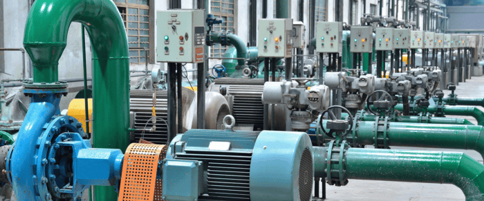 Row of industrial pumps and motors with green pipes and control panels in a factory setting, showcasing resilient water infrastructure designed for efficiency and reduced energy costs.