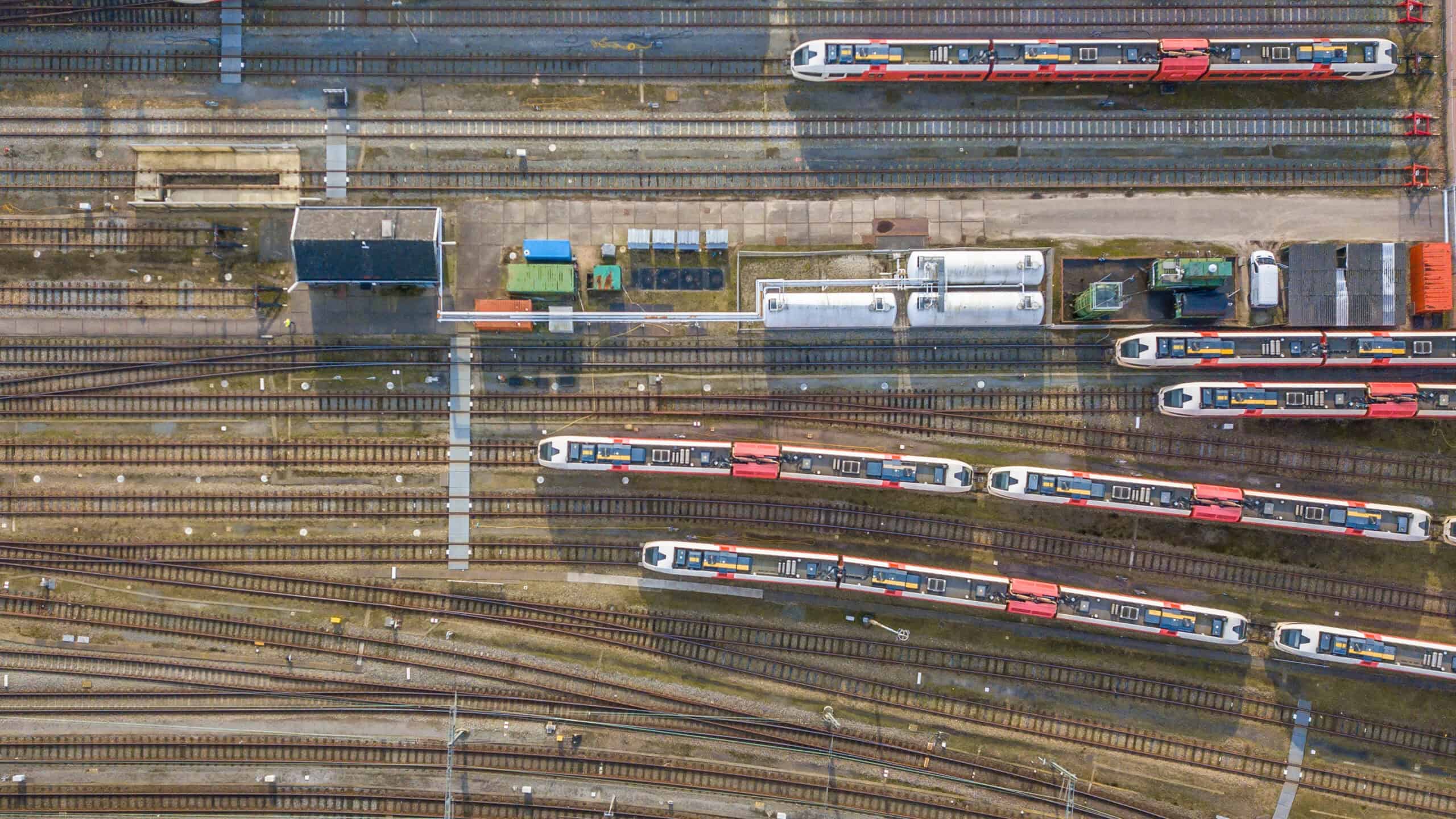 Aerial view of a train yard with multiple trains parked on parallel tracks, adjacent buildings, and various service equipment visible.