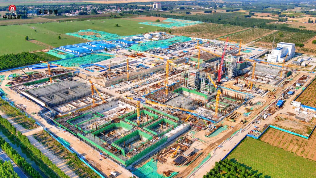 Aerial view of a large construction site in Xiong’an with multiple cranes, buildings in various stages of completion, and surrounding green fields—a vision of greener urban living for tomorrow’s cities.