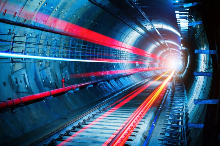 A brightly lit underground tunnel showcases blue walls and vibrant red, orange, and blue light trails stretching toward the tunnel's bright exit—capturing the spirit of overcoming an underground challenge.