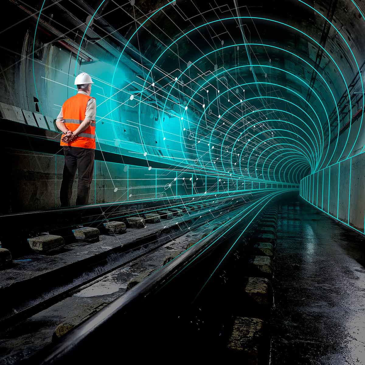 A person in a hard hat and safety vest stands on railroad tracks in a tunnel with digital grid lines and data network overlays.