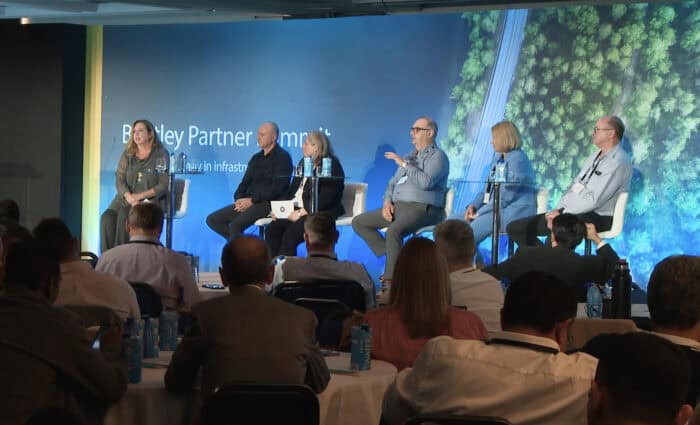 Panel of six people seated on a stage, speaking to an audience at the Bentley Partner Summit.