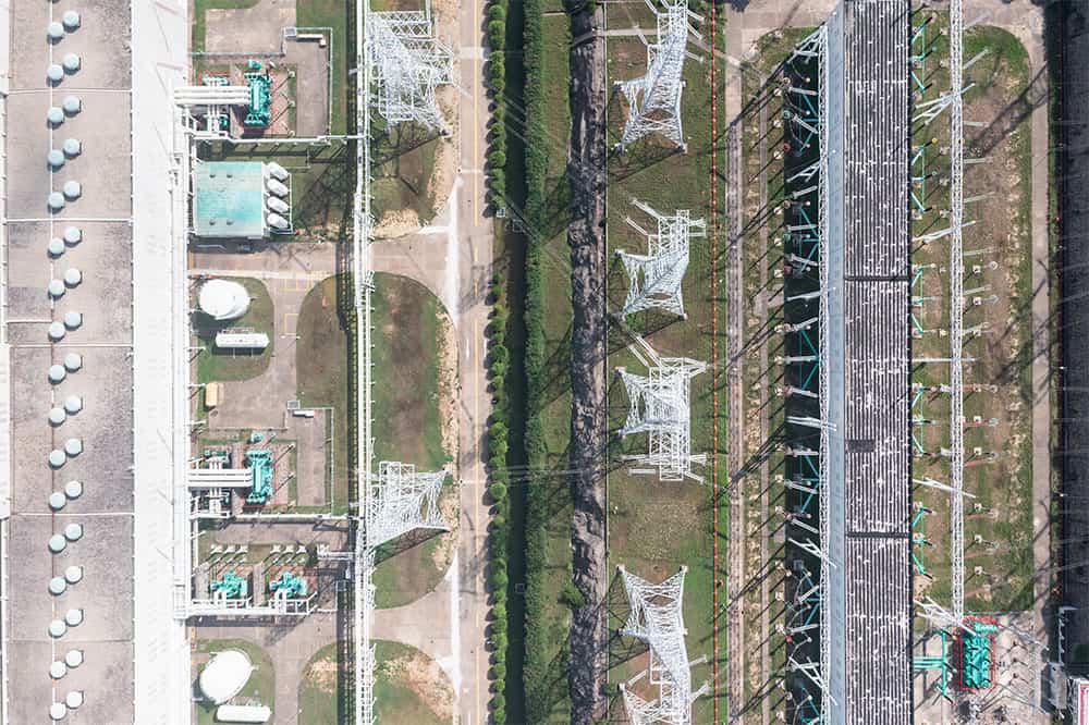 Aerial view of an industrial facility with machinery, tanks, and electrical grid structures divided by pathways and green areas.