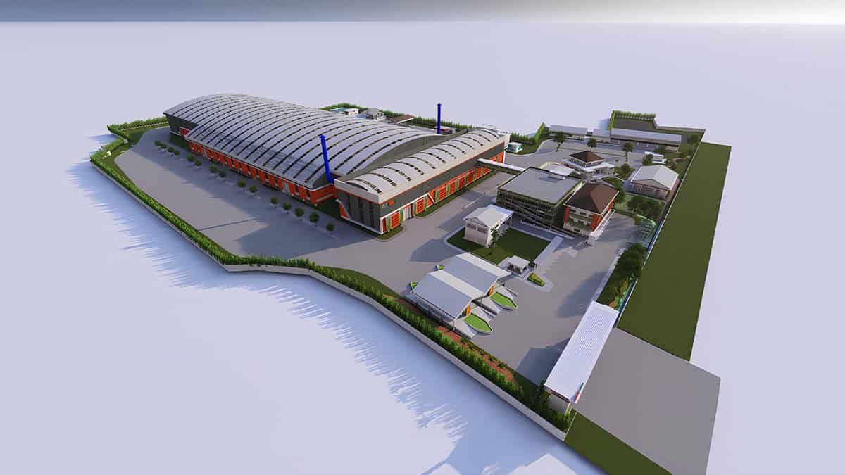 Aerial view of an industrial facility with a large warehouse, multiple smaller buildings, parking areas, and greenery within a fenced perimeter.