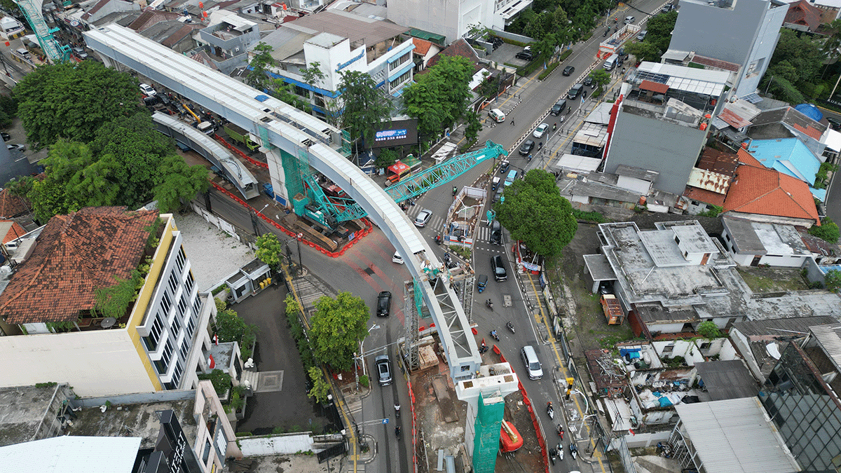 Aerial view of a city intersection with an elevated railway under construction, showing cranes, scaffolding, and vehicles moving on the surrounding roads.