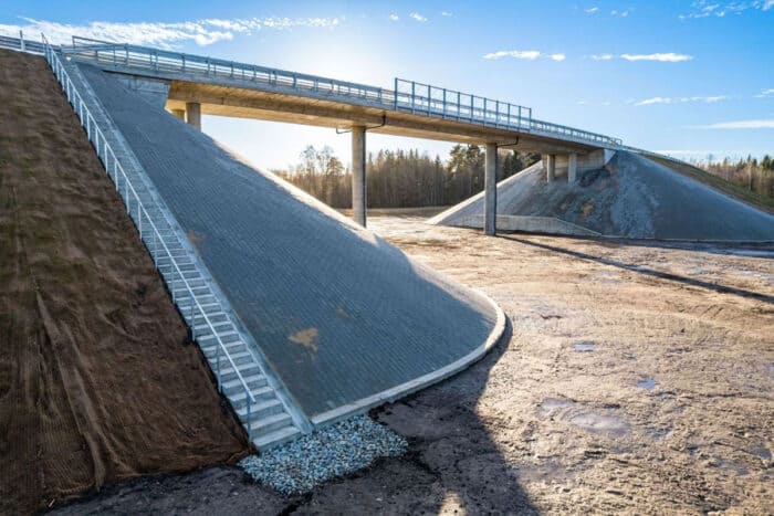 A concrete bridge with large sloped supports and surrounding earthworks on a clear day, with a blue sky in the background.