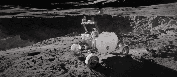 A lunar rover with NASA logos is parked on a rocky, cratered surface of the Moon under a dark sky.