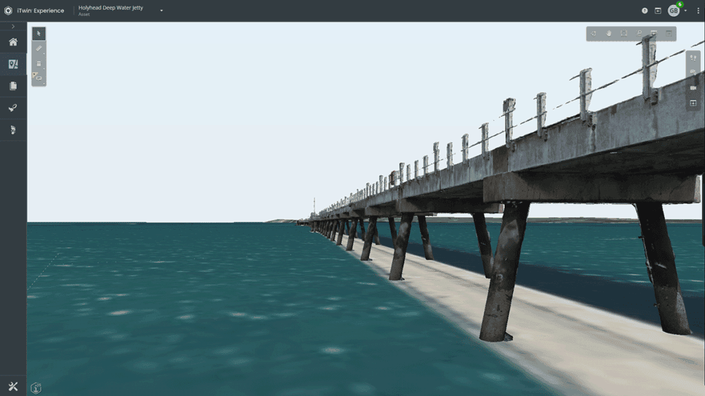 A concrete pier with metal railings extends over blue-green water toward a distant shoreline under a clear sky, reminiscent of structures seen in Holyhead Jetty inspection projects by Royal HaskoningDHV.