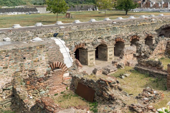 Ancient stone ruins with arched openings and scattered greenery under a partly cloudy sky.