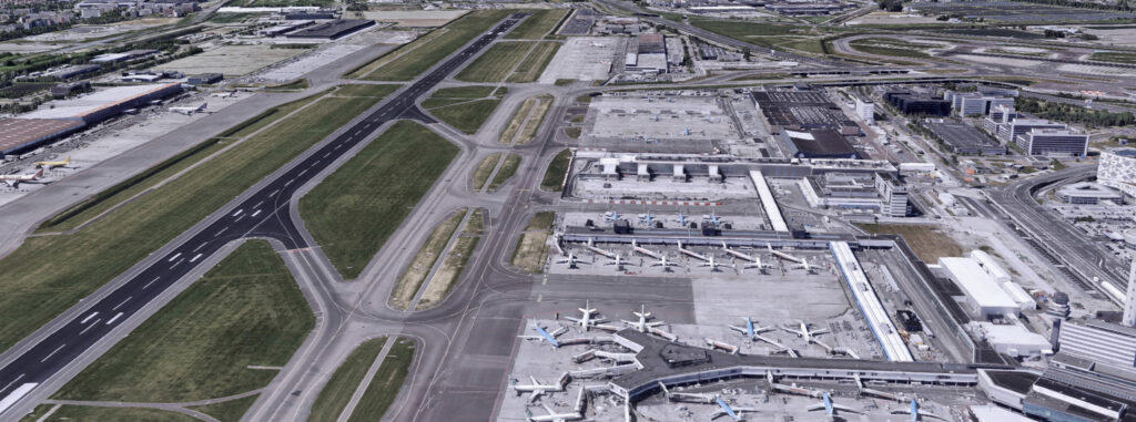 Aerial 3D view of an airport in the Netherlands, showing multiple taxiways, runways, terminals, and several airplanes parked at gates near the sea.