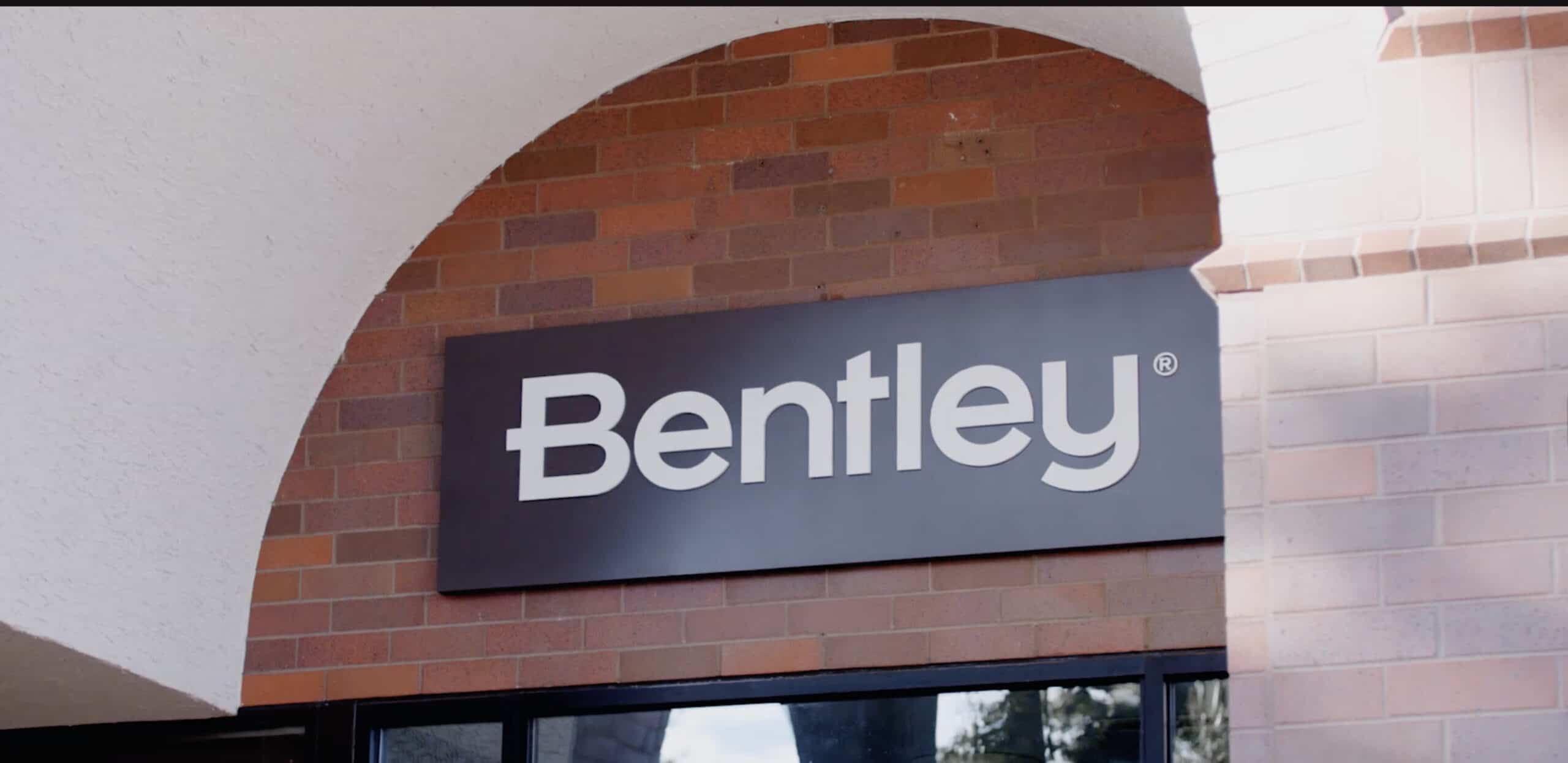 A rectangular Bentley sign with white letters is mounted on a brick wall above a building entrance, highlighting the company’s innovation in AI in civil engineering.