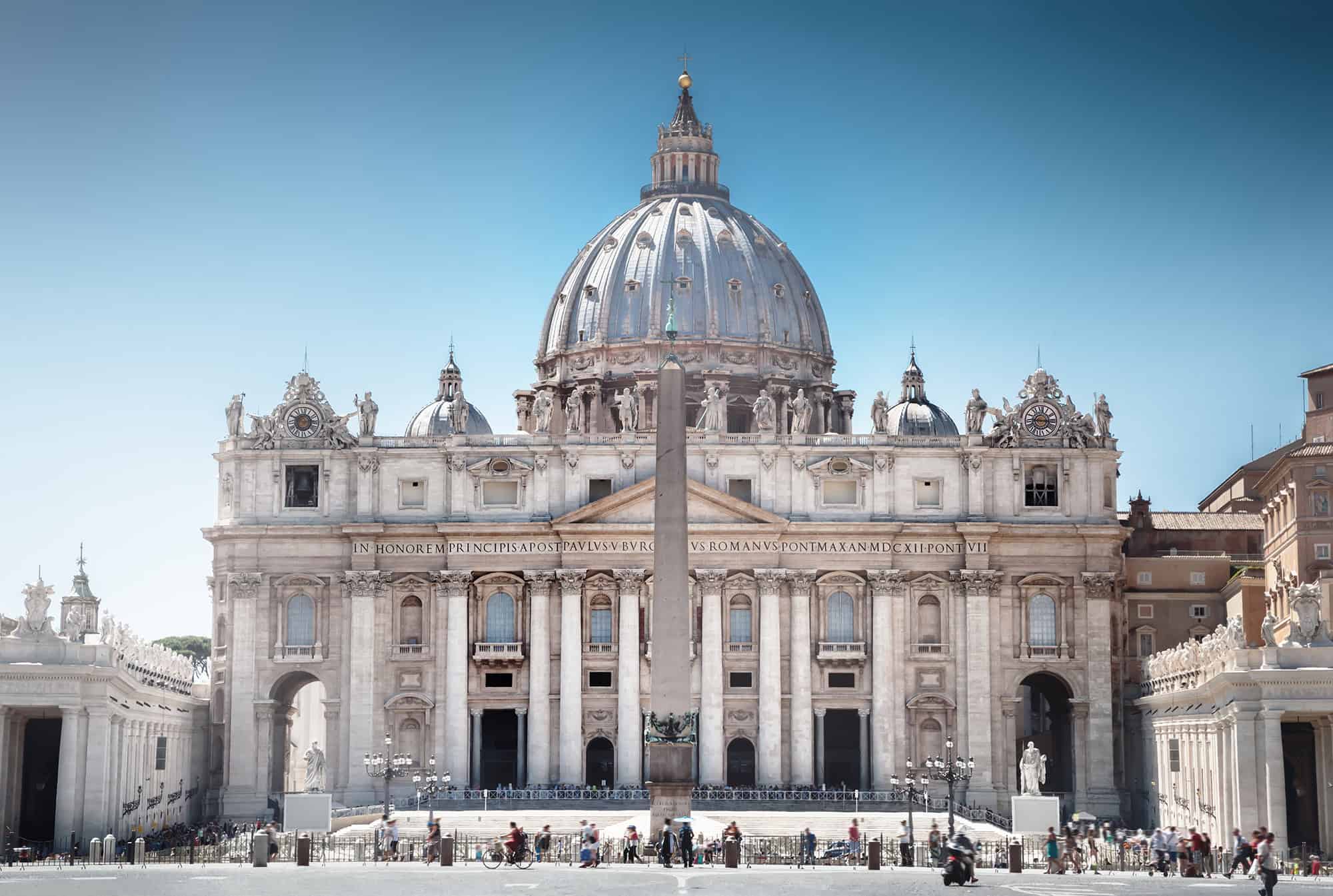 St. Peter's Basilica with a central obelisk in St. Peter's Square, Vatican City, under a clear blue sky.