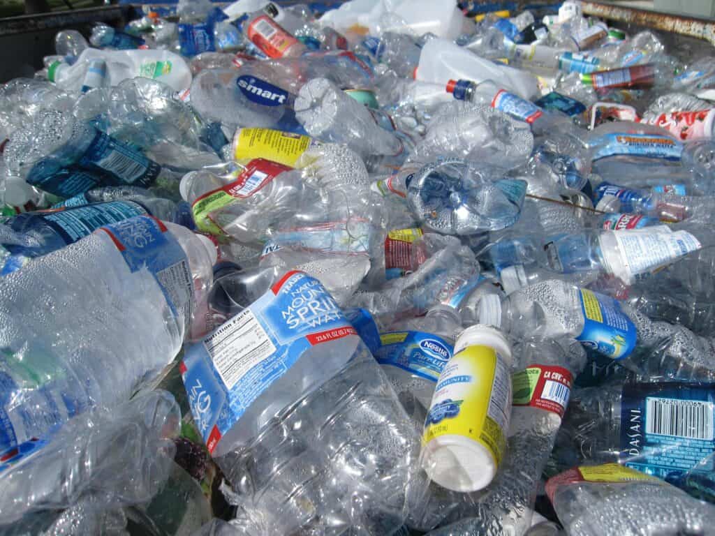 A large pile of empty, crushed plastic bottles and containers, mostly water bottles, collected together for recycling or disposal—a striking image in today's rubble economy.