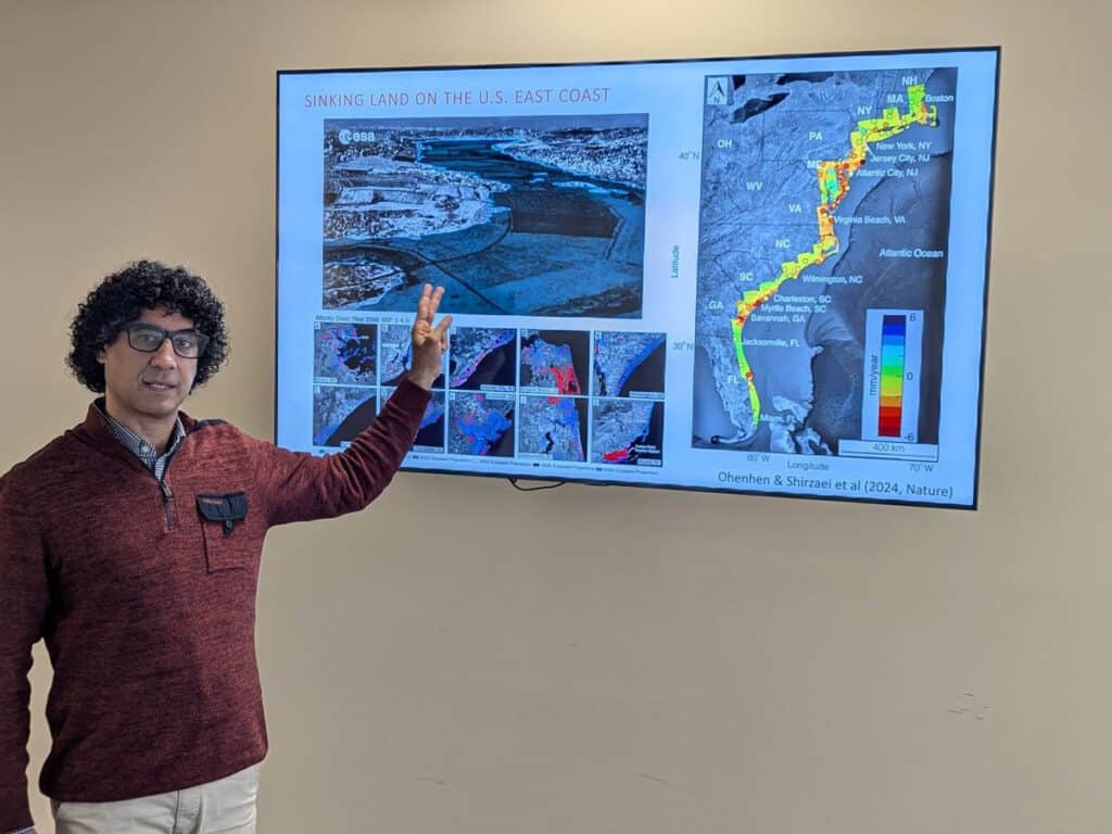 A person gestures towards a slide presentation on "Sinking Land on the U.S. East Coast," featuring maps and data visuals.