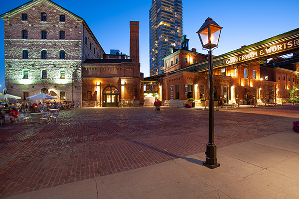 A cobblestone courtyard surrounded by historic brick buildings, with outdoor seating and a tall streetlamp at dusk—reflecting Toronto rail safety and transportation innovation in the city’s timeless charm.