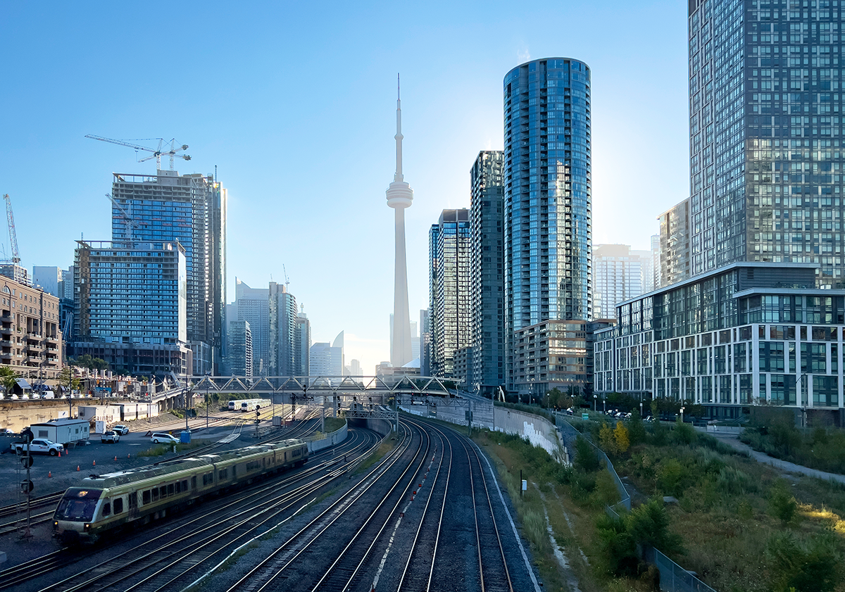Downtown Toronto cityscape with train tracks and advanced rail protection in the foreground, modern high-rise buildings, and the CN Tower visible in the center background under a clear sky—showcasing Toronto rail safety innovators at work.