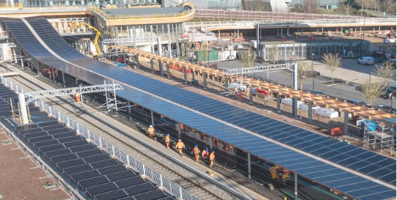 A railway station with multiple train tracks covered by large solar panels, featuring the Arcadis Rail Division’s commitment to engineering clarity as several workers in orange vests walk along the tracks.
