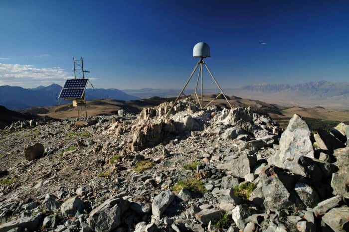 A rugged rocky landscape with a solar panel and a weather monitoring device installed on a mountaintop under a clear blue sky.