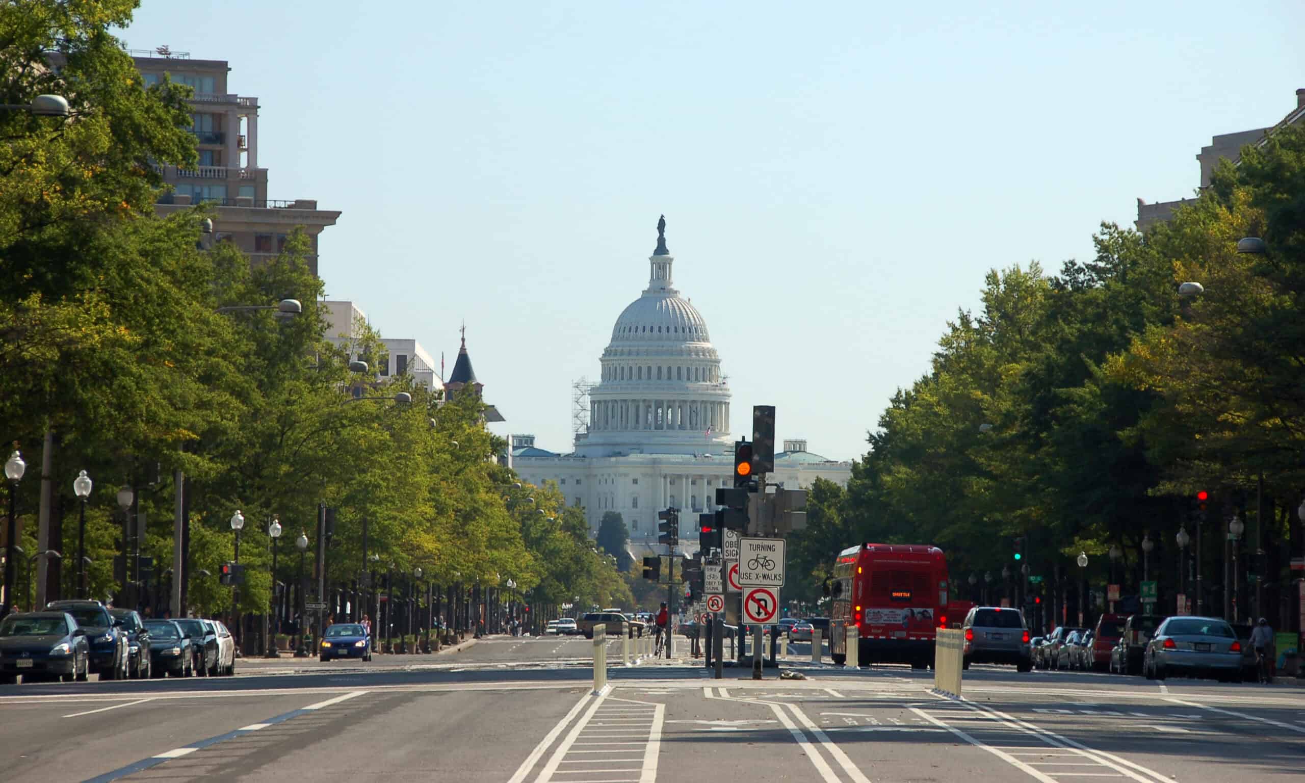 View of the United States Capitol building from a city street with trees, vehicles, and traffic signals in the foreground.