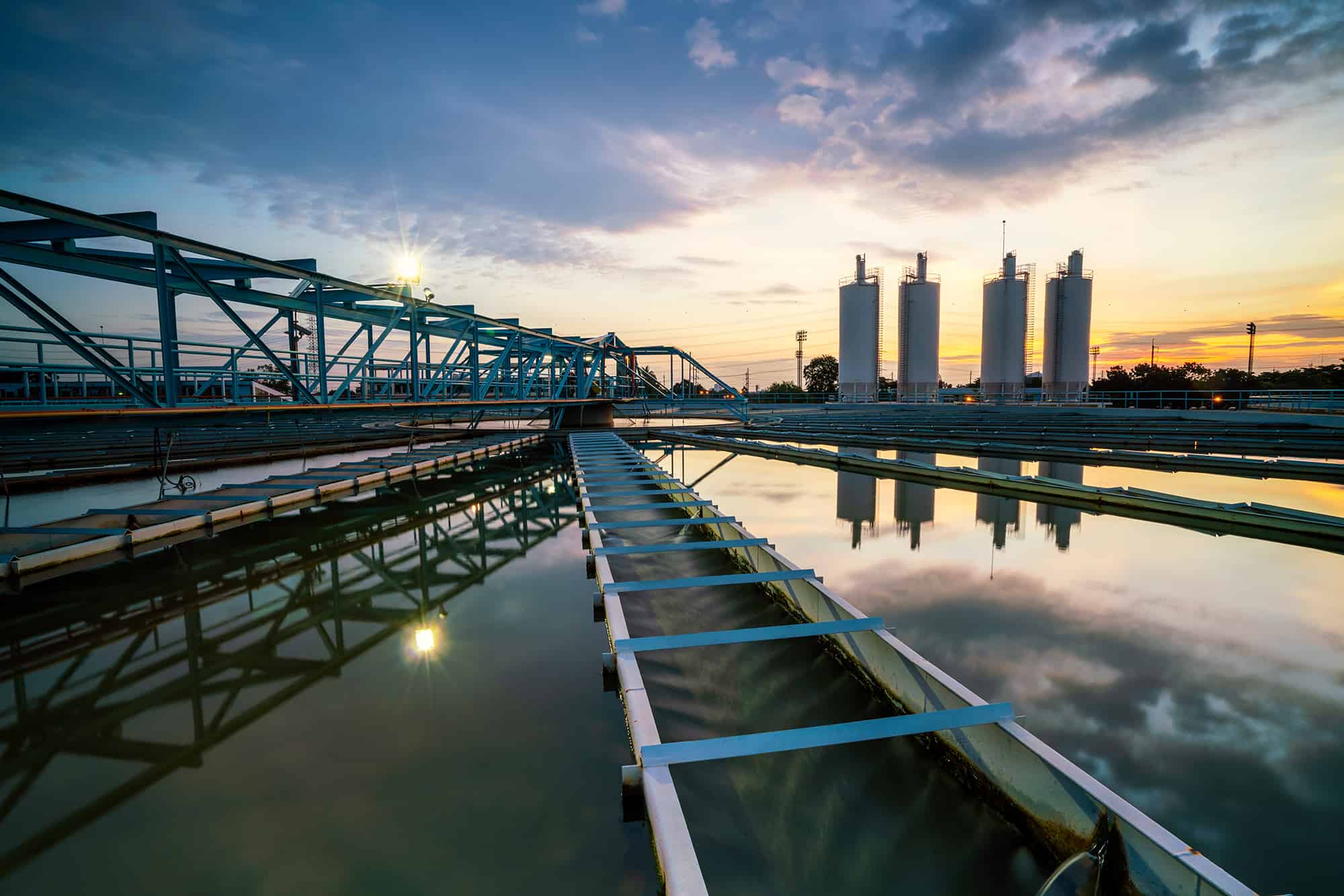 A water treatment plant at sunset with reflection in the water and a dramatic sky.