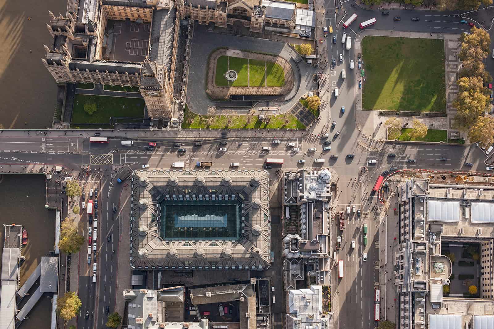 Aerial view of a busy city intersection in London, where smart mobility integrates roads, vehicles, green spaces, and historic buildings like the Palace of Westminster—highlighting the evolution of modern cities.