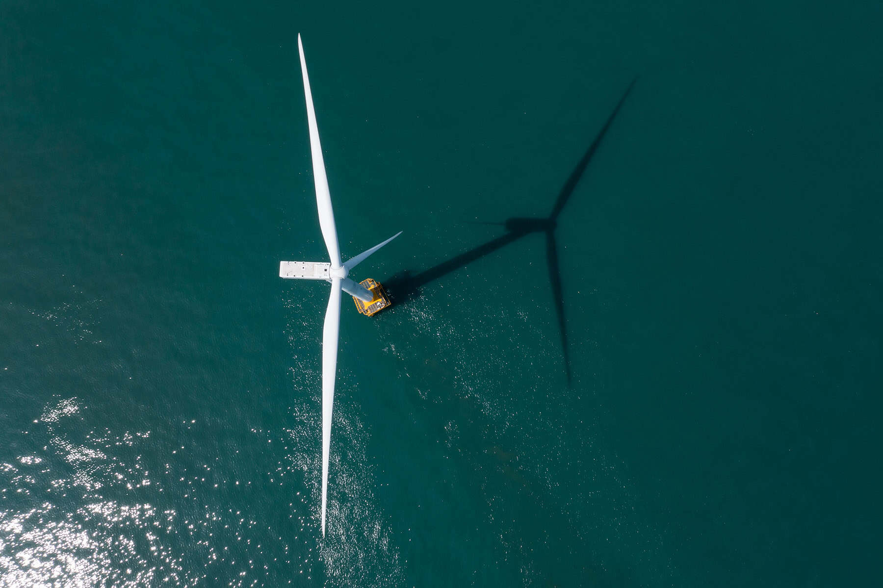 Aerial view of an offshore wind turbine with a maintenance vessel nearby, casting a long shadow across the water—ideal for integrating substation data to optimize operations and ensure efficient energy transmission.