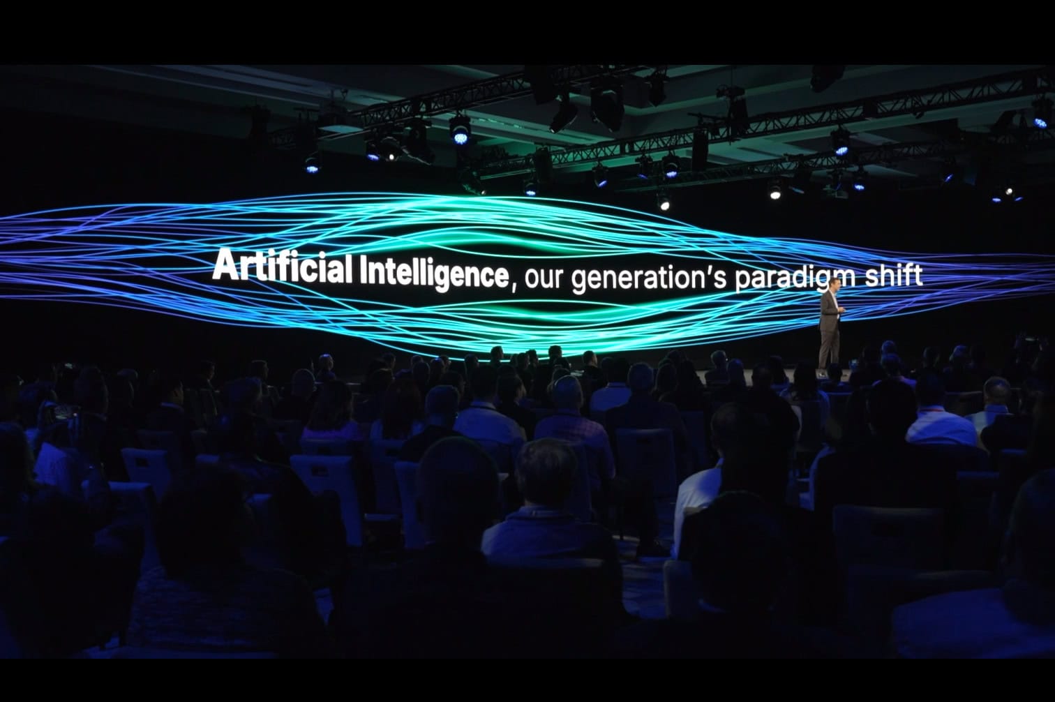 Bentley Chief Executive Officer Nicolas Cumins on stage with a large digital backdrop displaying "Artificial Intelligence, our generation's paradigm shift" to an audience at a conference.