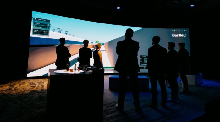 People in a dark room stand facing a large screen displaying a virtual design interface with "Bentley" in the corner.