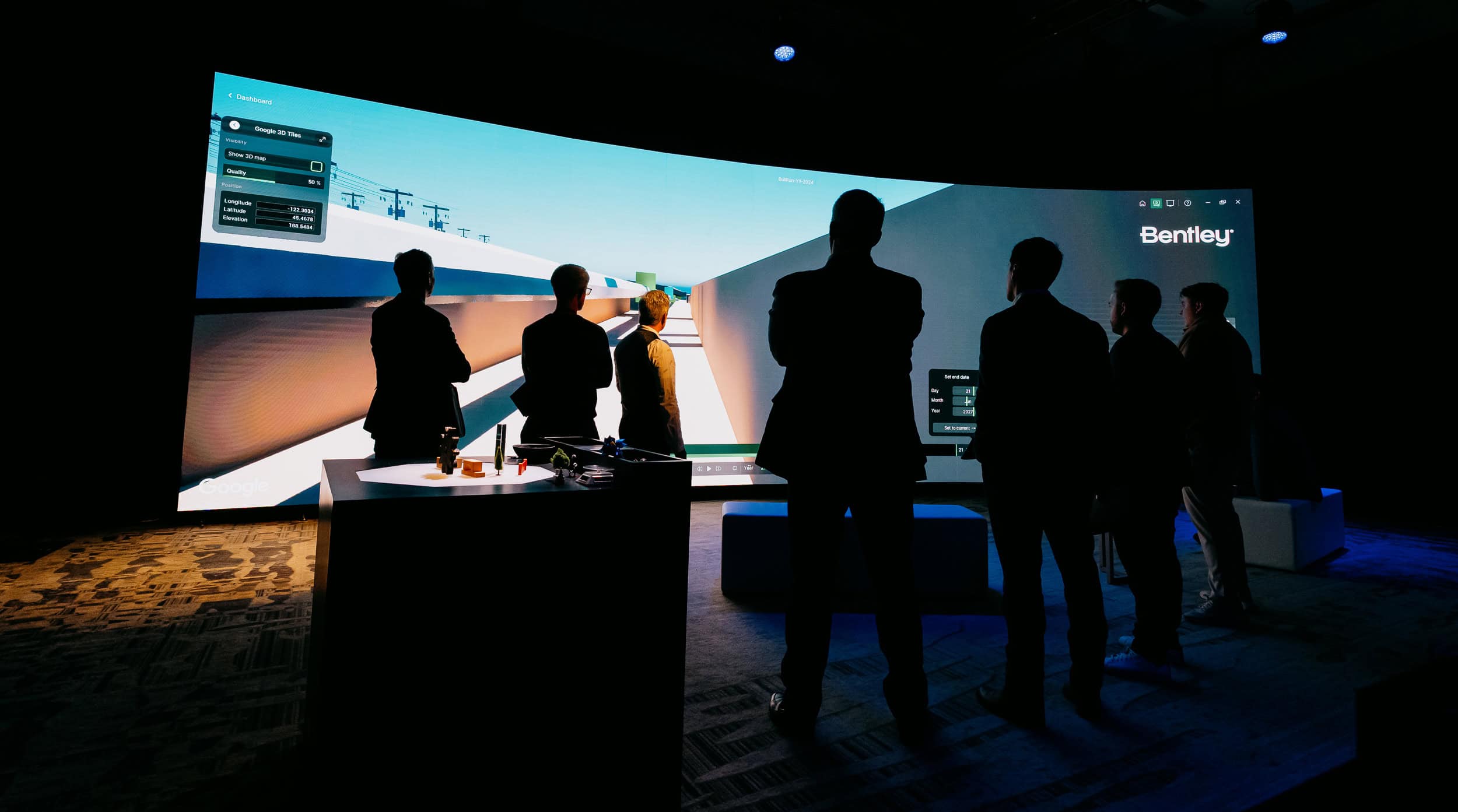 People in a dark room stand facing a large screen displaying a virtual design interface with "Bentley" in the corner.